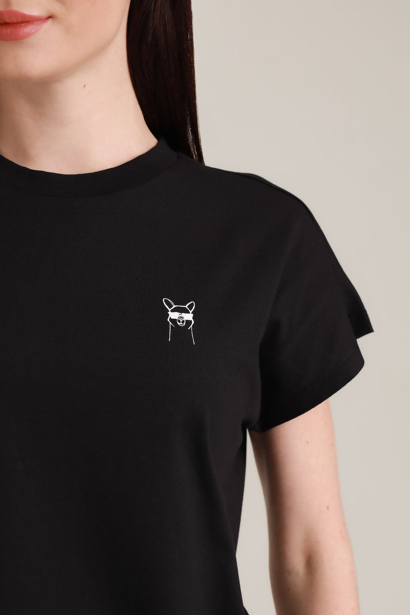 Close Up von Frau in fairem T-Shirt in Schwarz mit Cool Paka-Motiv über der linken Brust. Das Motiv besteht aus weißem Siebdruck. Foto von Ungerade Wien