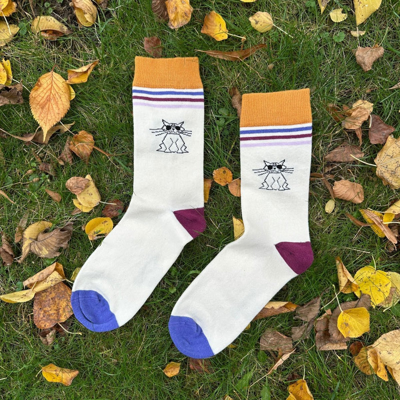 Cool Cat Stripes – Bio-Baumwollsocken mit Streifen & Katzen-Attitüde - Der Saum ist gold-gelb (ca.4cm breit), darunter befinden sich 3x 5mm breite Streifen in blau, rot und dunkellila. Zwischen den Streifen und der Ferse (Knöchel) befindet sich der Druck der Katze mit Sonnenbrille in Schwarz. Die Ferse ist rot und die Sockenspitze dunkellila. Produktfoto von Ungerade Wien