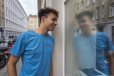 Mann in nachhaltigem blauen Shirt vor Fenster in Wien